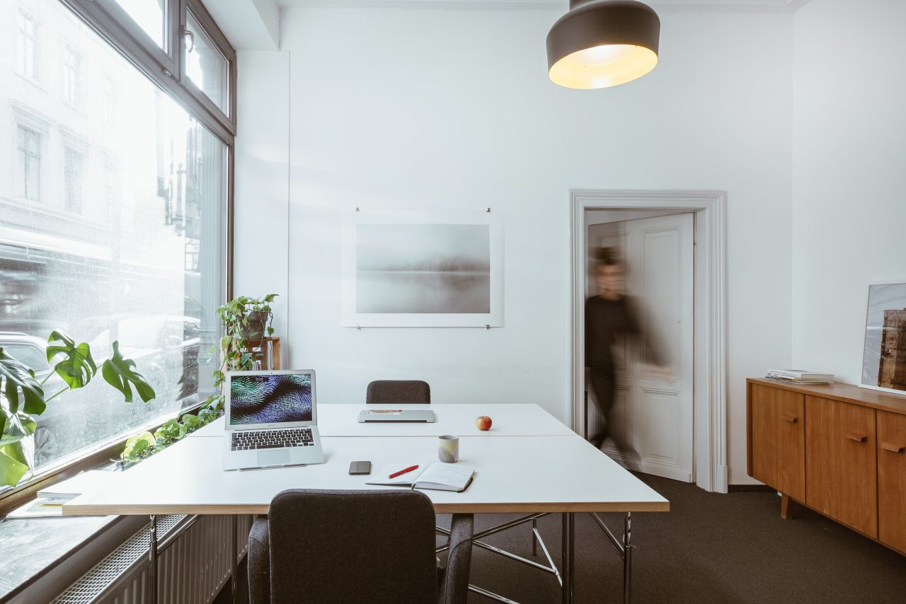 Heller Besprechungsraum mit großem Fenster, weißem Tisch, Monstera und Holzsideboard
