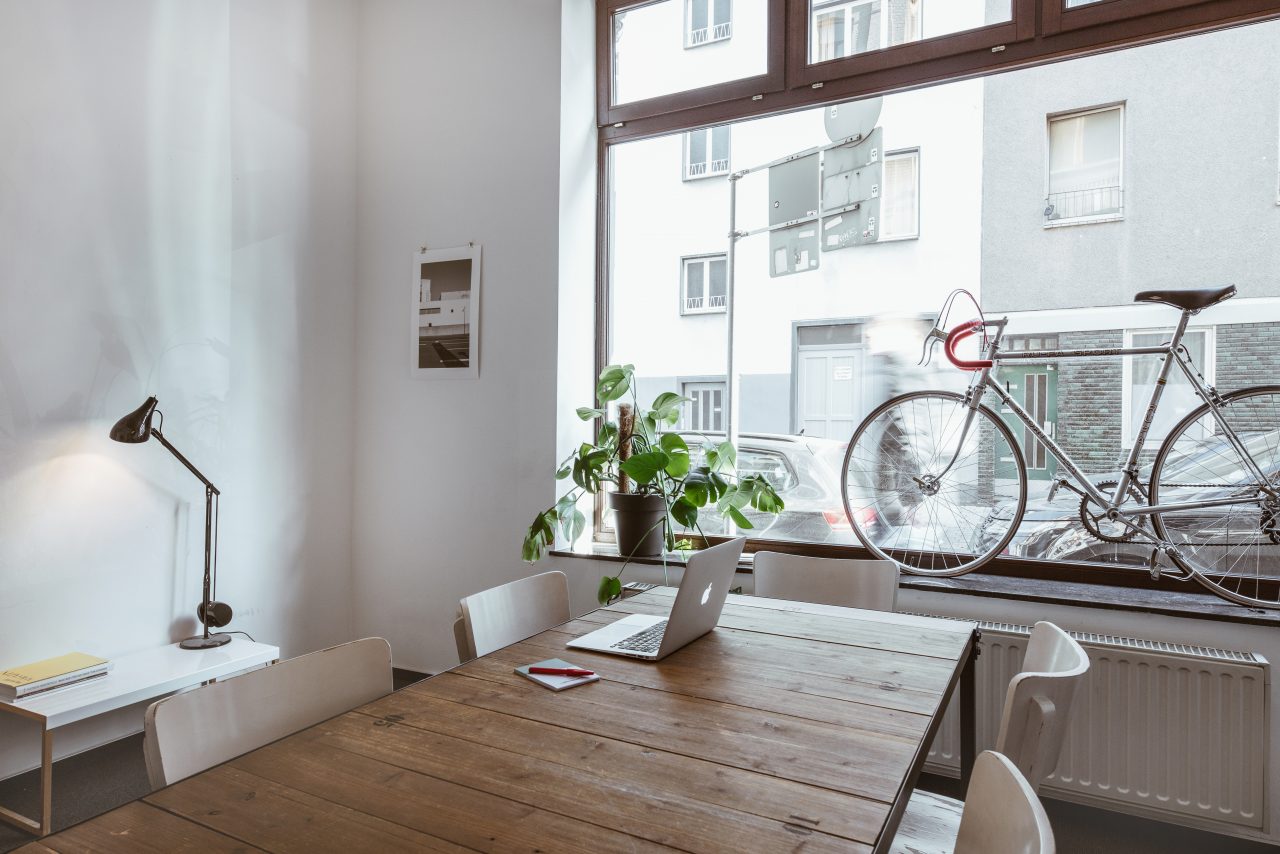 Holztisch am Schaufenster mit Monstera und einem silbernen Rennrad im Fenster